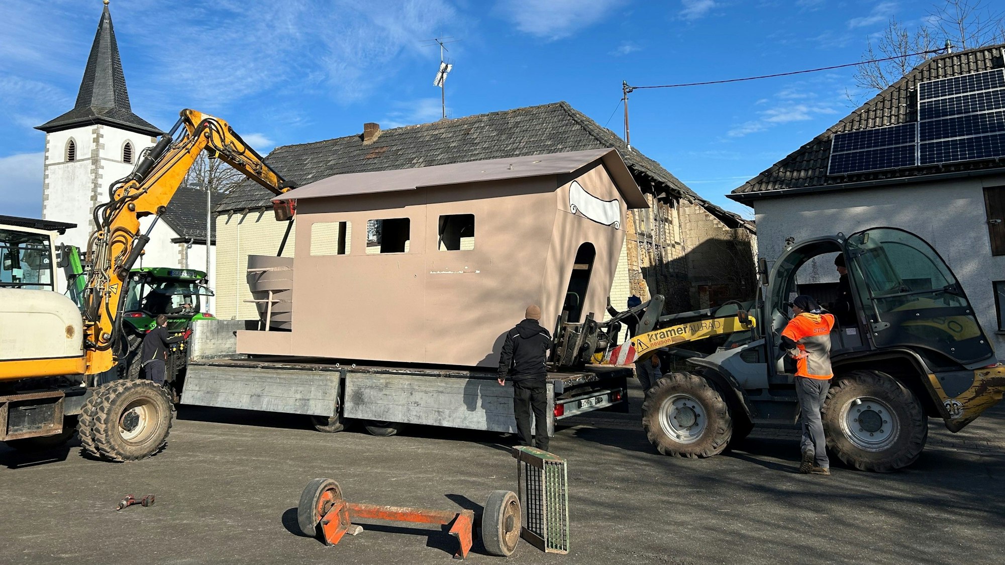Ein Karnevalswagen wird in Nettersheim-Roderath mit Baggern auf einen neuen fahrbahren Untersatz gehoben.
